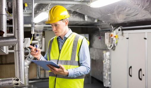 Mann mit Sicherheitsweste und Helm prüft technische Anlage