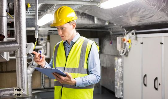 Mann mit Sicherheitsweste und Helm prüft technische Anlage