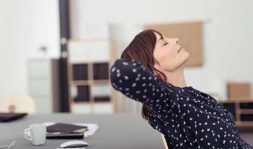 Frau sitzt entspannt und zurückgelehnt am Schreibtisch