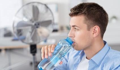 Genug trinken! mann trinkt wasser im büro mit ventilator im hintergrund