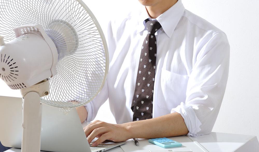 Hitzeschutz am Arbeitsplatz Mann sitzt am Schreibtisch vor einem Ventilator
