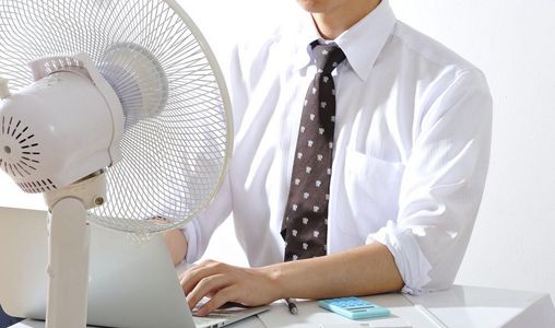 Hitzeschutz am Arbeitsplatz Mann sitzt am Schreibtisch vor einem Ventilator