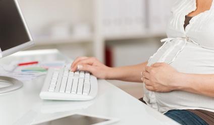 Schwangere Frau sitzt am Computer.